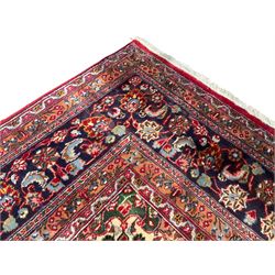 Large Persian Kashan crimson ground carpet, the busy field decorated with a central floral pole medallion surrounded by stylised plant motifs and palmettes with contrasting indigo spandrels, the guarded border decorated with repeating connected foliate designs