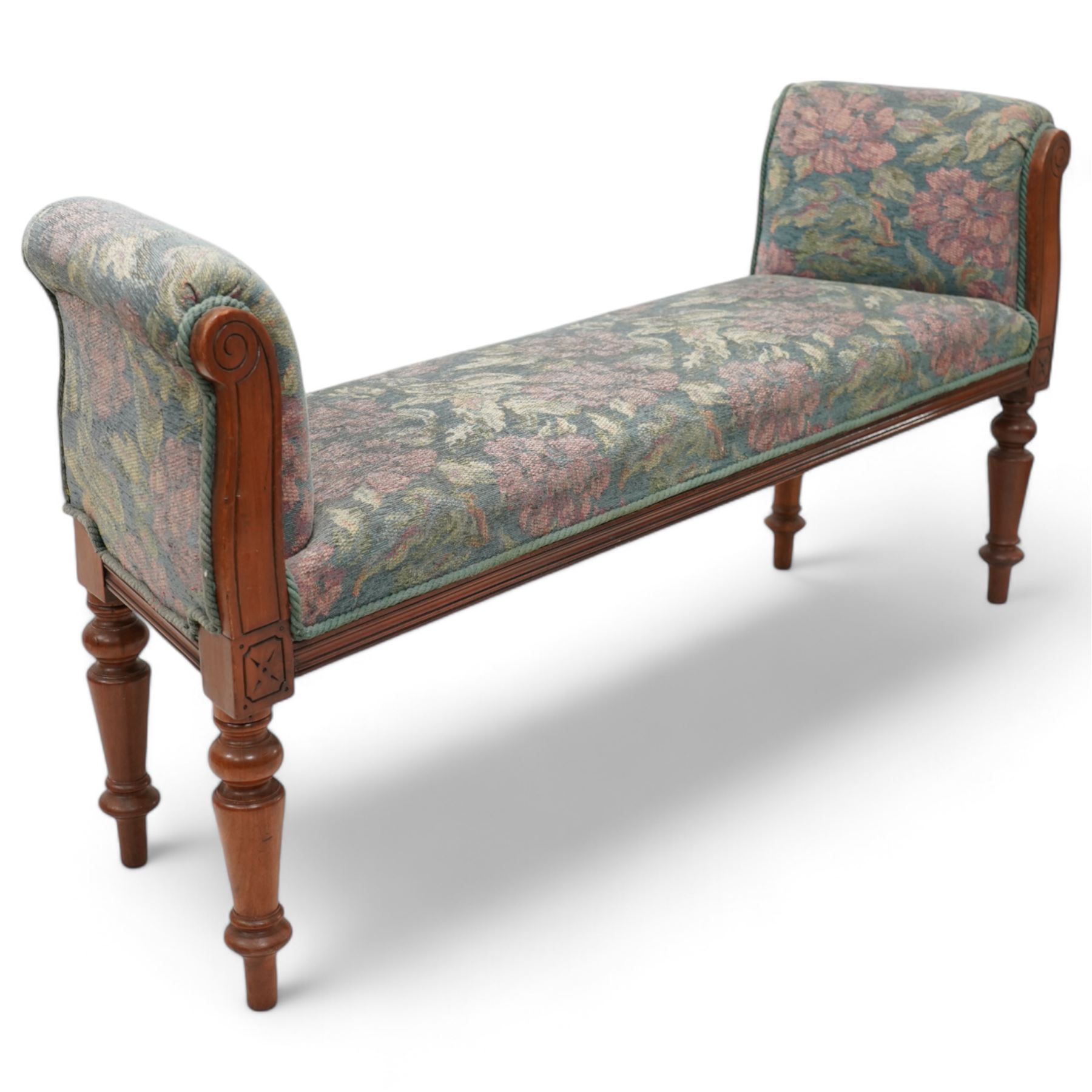 19th century mahogany framed bay window seat of tapered form, rolled arms decorated with carved scrolling, seat and arms upholstered in indigo ground floral patterned fabric, moulded lower rail over turned supports