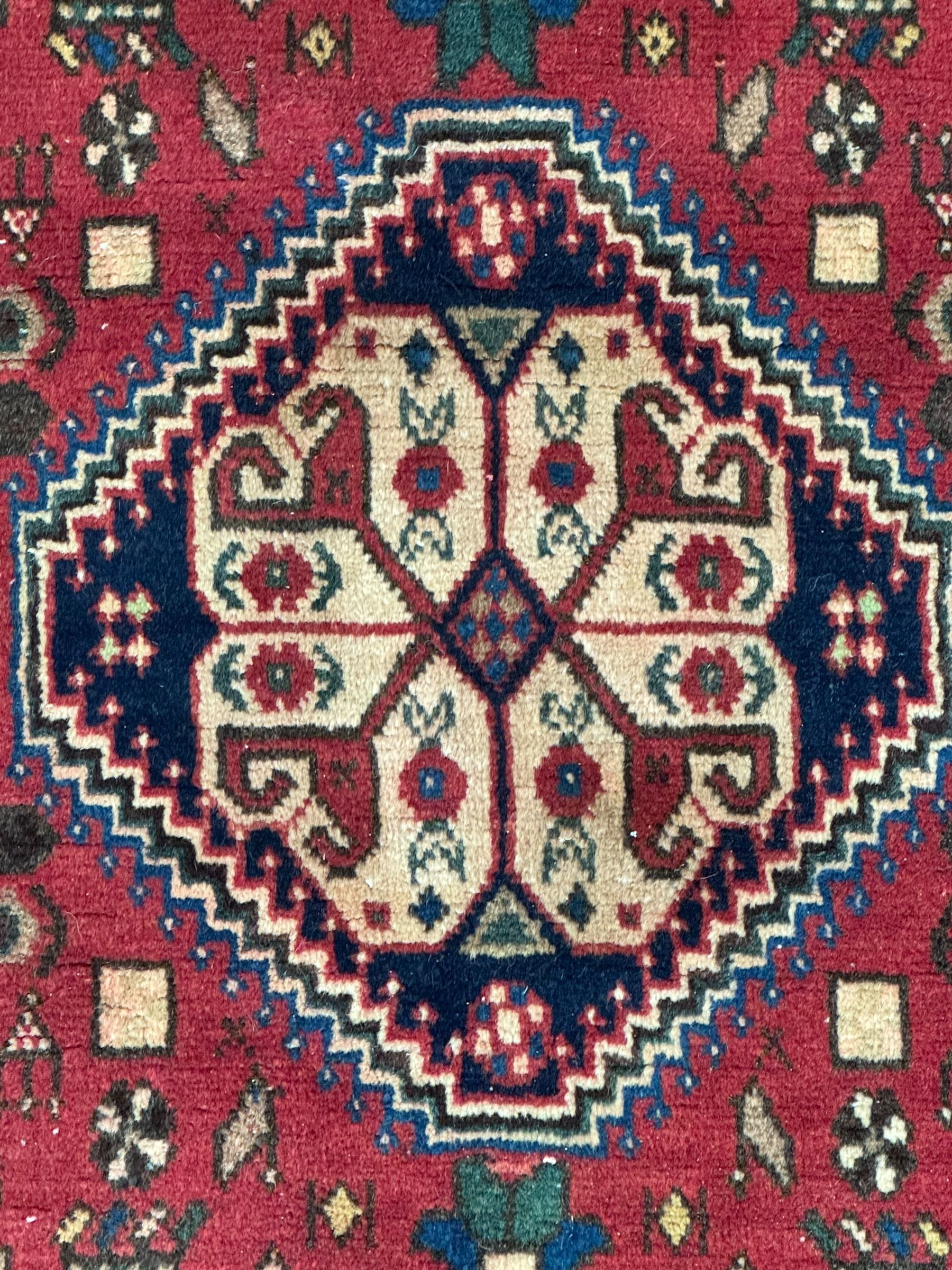 South West Persian Abadeh crimson ground rug, indigo ground with crimson lozenge field, decorated all over with small stylised motifs of flowerheads, hooks, animals and birds, guarded border decorated with trailing leaves and stylised plant motifs 