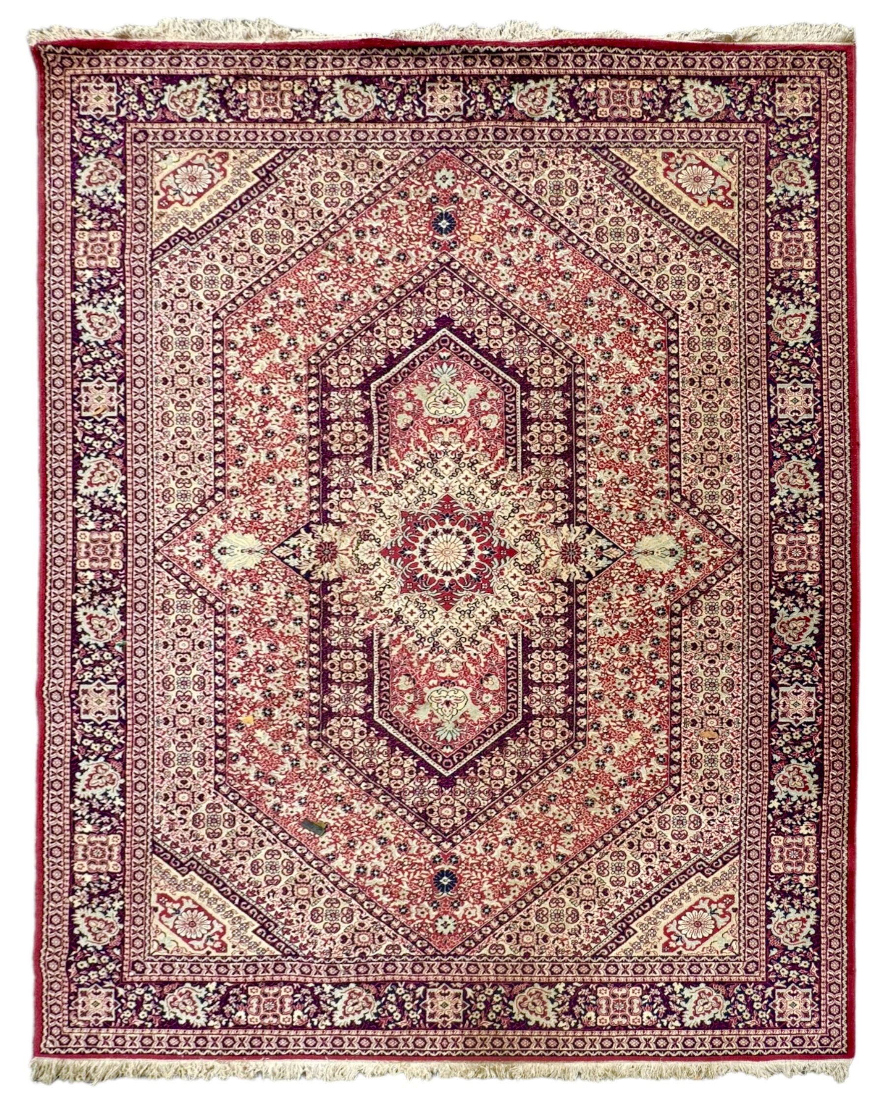 Persian Heriz design red ground carpet, the field decorated with a central star-shaped medallion surrounded by geometric floral motifs and angular vine patterns, the spandrels highlighted with palmette designs, the main border featuring a series of stylised rosettes and leaves against a dark blue ground, enclosed by multiple guard stripes with alternating floral and geometric motifs