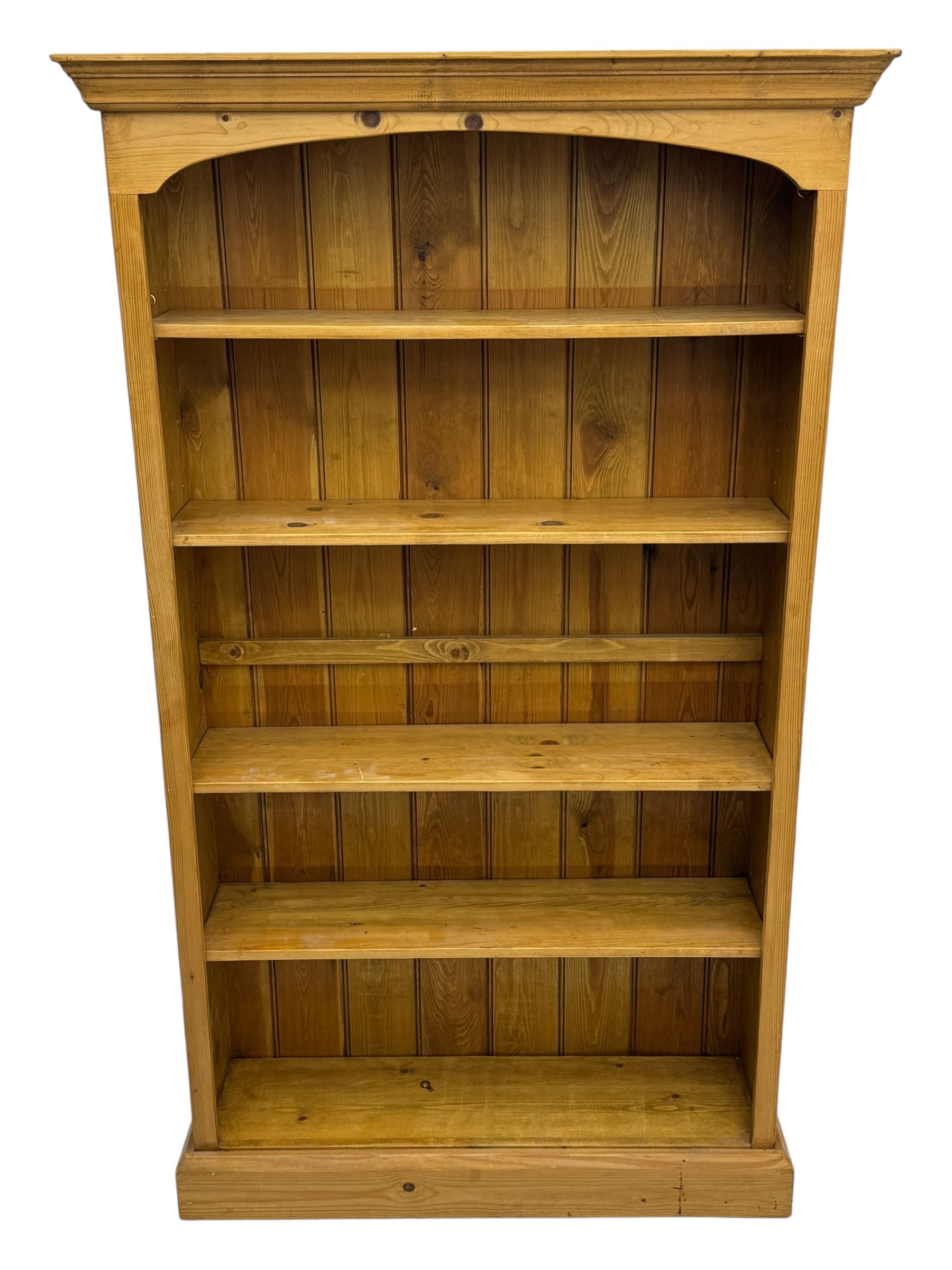 Pine open bookcase, projecting moulded cornice over arched frieze, fitted with four adjustable shelves, on plinth base