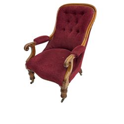 Victorian mahogany framed open armchair, upholstered in buttoned red fabric, the arm terminals carved with scrolls, on turned front supports with brass cups and castors