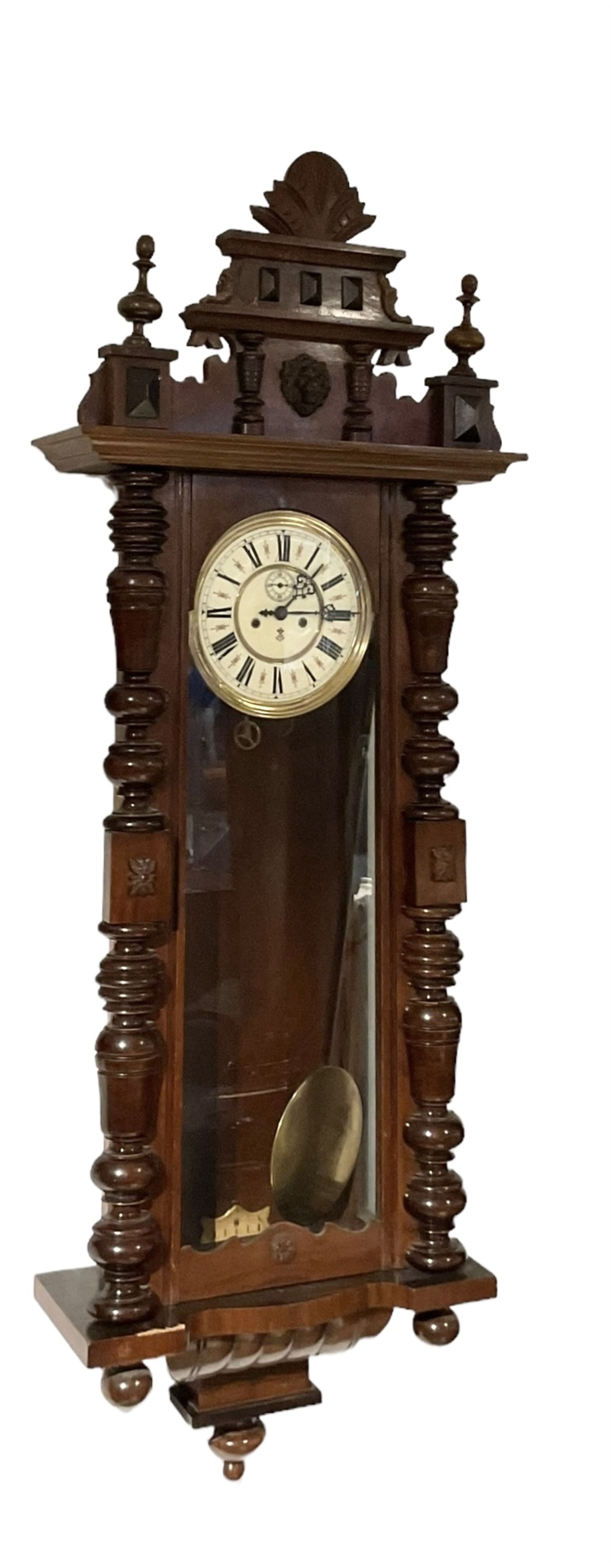 Gustav Becker -  German weight-driven 8-day wall clock in a walnut and ebonised case with a carved pediment and finials, fully glazed case door with visible pendulum and two brass cased weights, two  part dial with seconds hand, Roman numerals and pierced steel hands, rack striking movement with a deadbeat escapement.