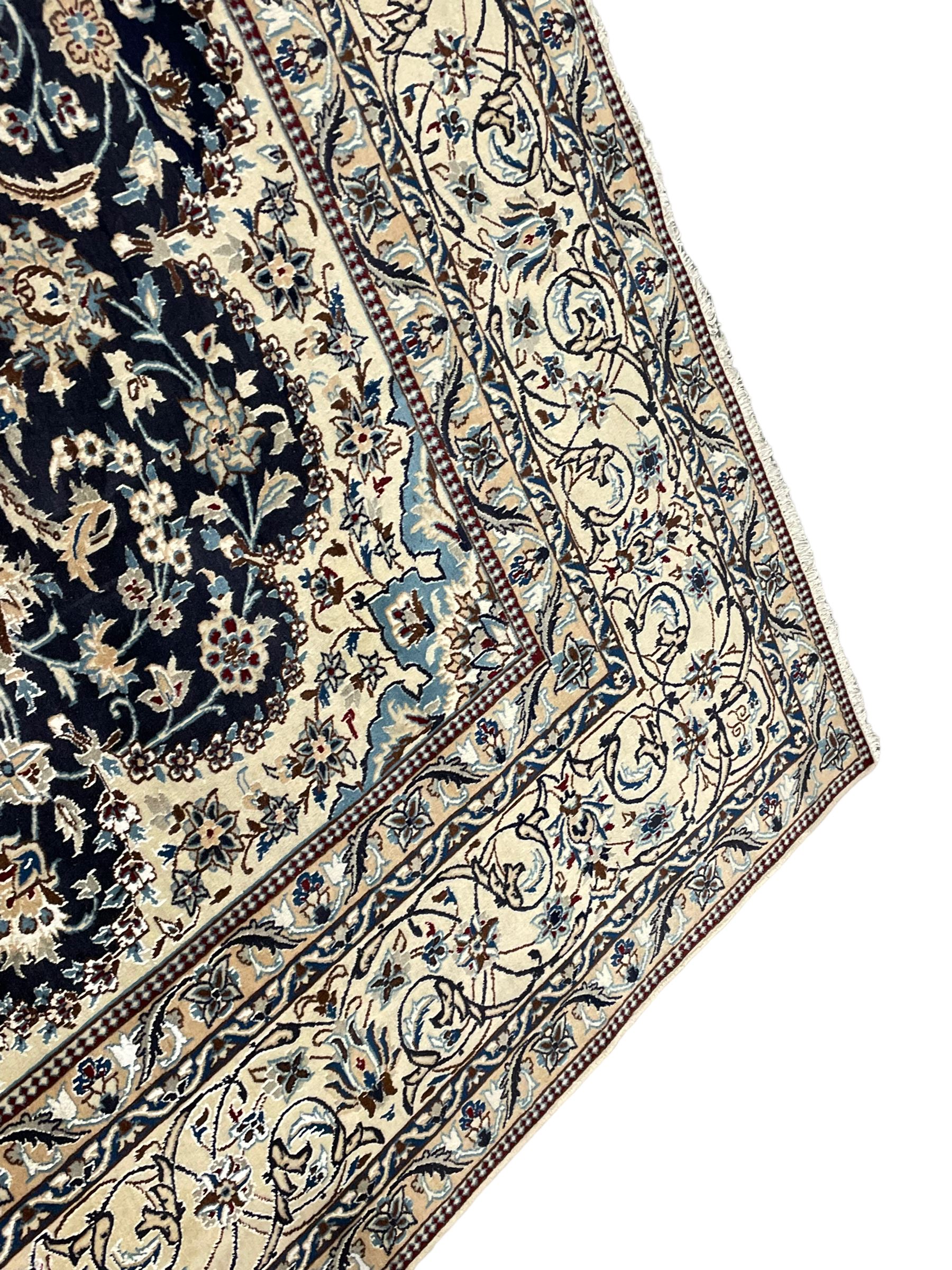 Persian Kashan indigo ground carpet, the central ivory rosette medallion surrounded by trailing and interlaced flower heads and branches, matching spandrels with floral design, the border with scrolling pattern decorated with stylised plant motifs within guards