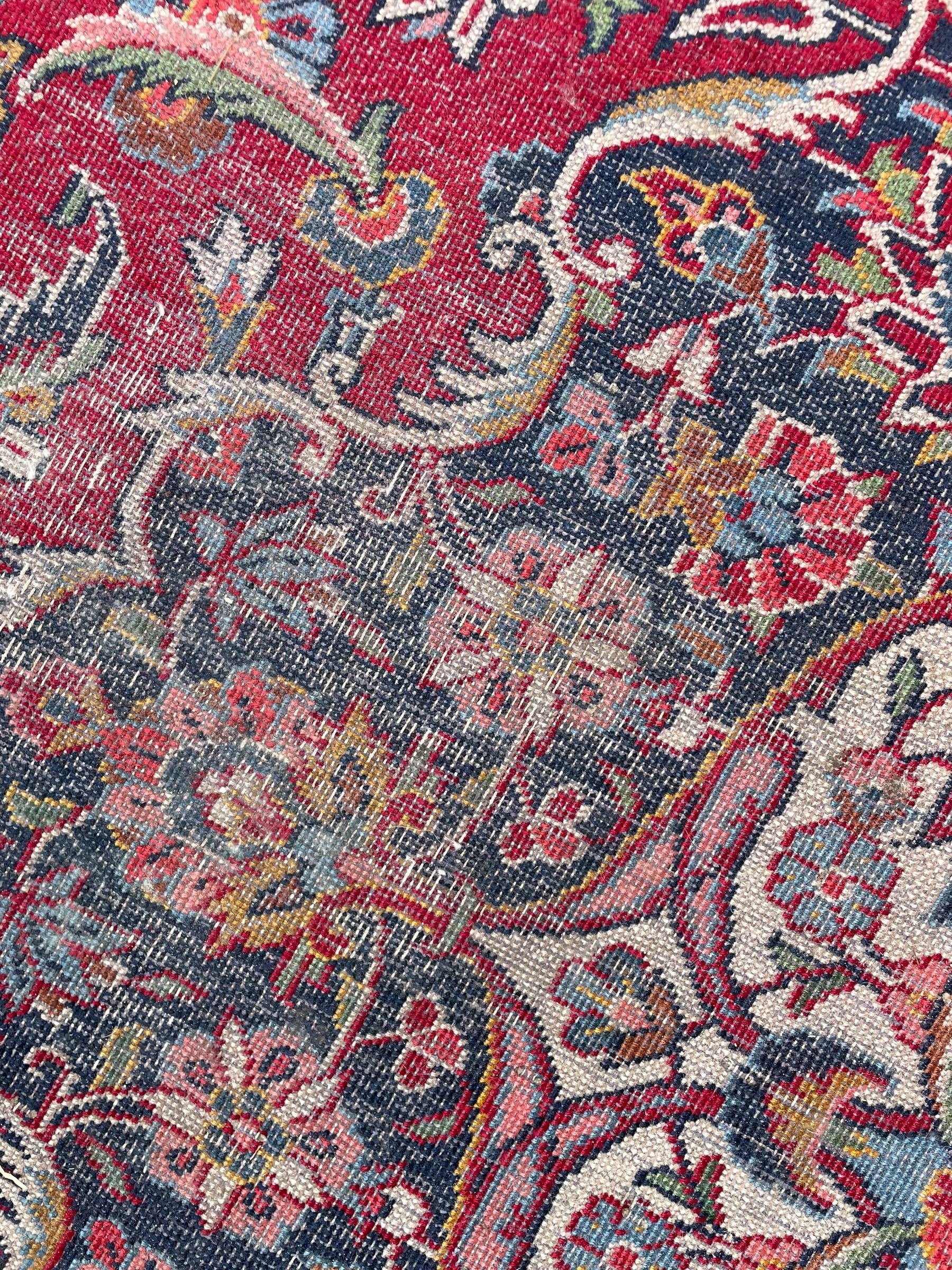 Large Persian Kashan crimson ground carpet, central floral medallion surrounded by swirling leafy branches and palmettes, enclose by floral pattern spandrels, the indigo border with overall scrolling design decorated with palmettes, within guard stripes 