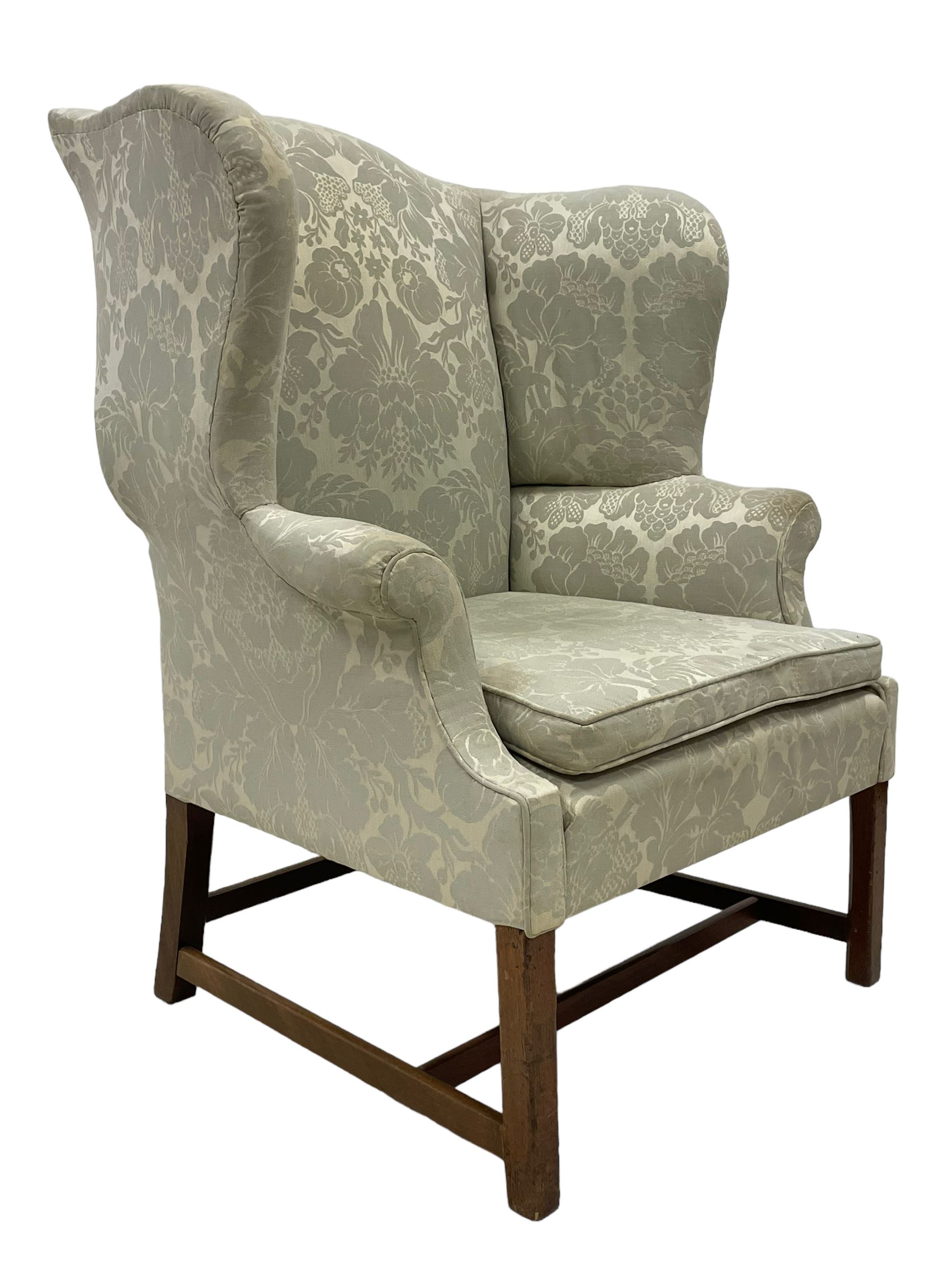 Georgian mahogany framed wingback armchair, upholstered in floral pattern silk damask fabric, wide seat enclosed by rolled arms, on chamfered square supports united by plain stretchers 