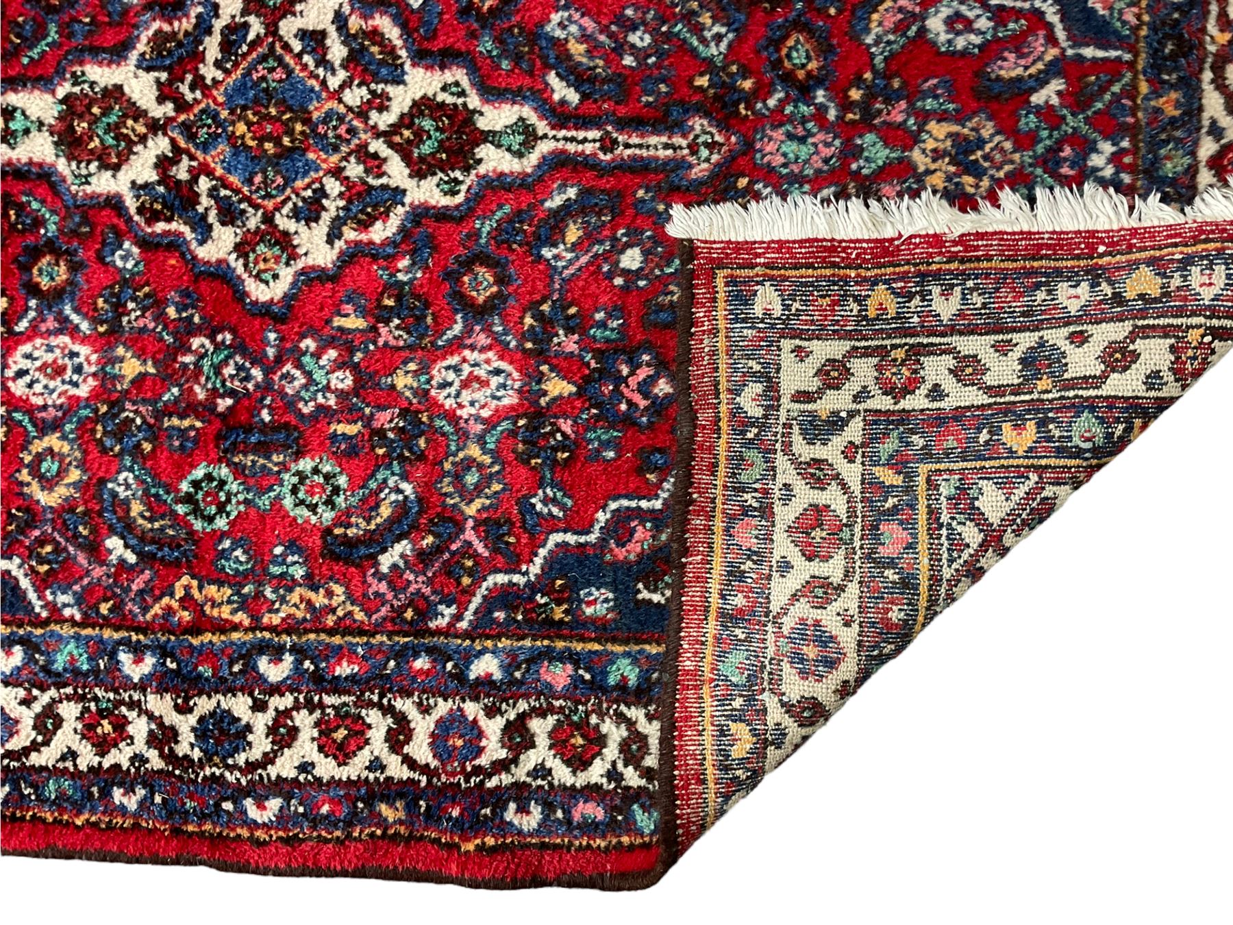 Persian Herati crimson ground rug, central ivory pole medallion surrounded by Herati motifs, with contrasting indigo spandrels, multi-band border with interlaced flowerheads