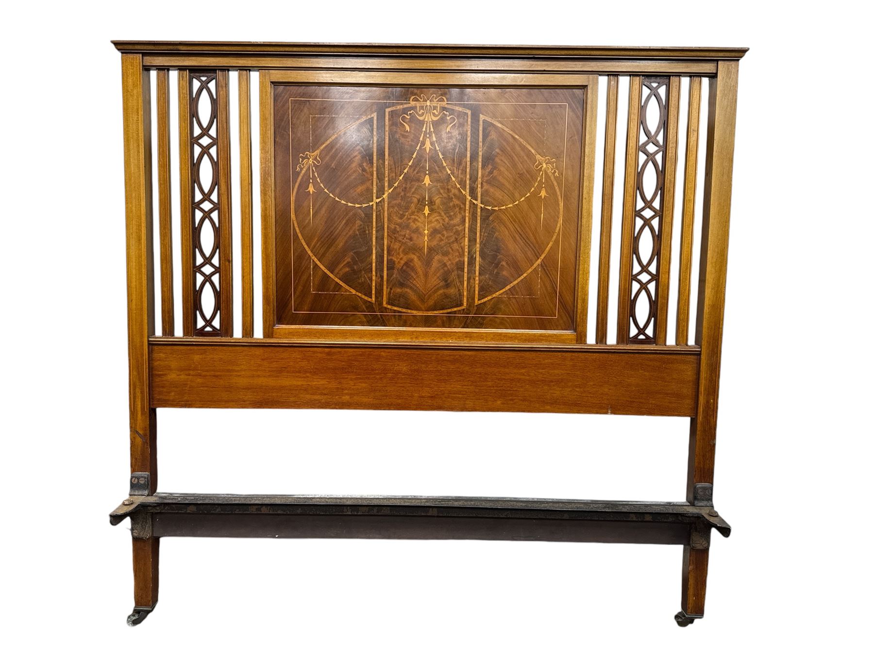 Edwardian mahogany double bedstead, the headboard with central book-matched mahogany panel, decorated with satinwood inlaid swags and ribbons, flanked by openwork carved vertical supports, complete with matching footboard and folding upholstered base