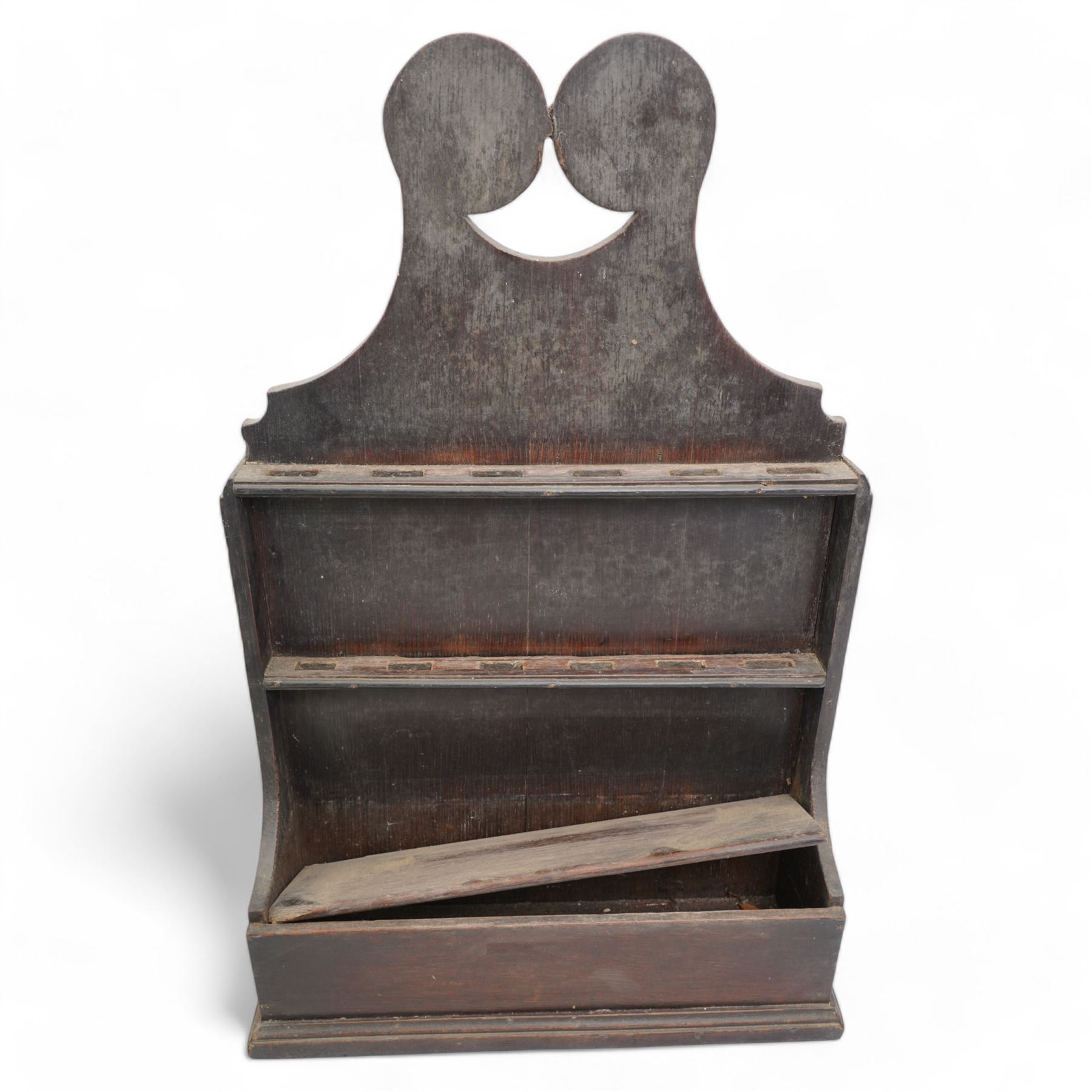 An 18th century provincial oak spoon rack, the scroll carved pediment over two six-hole racks, with candlestick compartment to base, H61cm