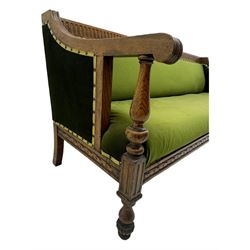 Late Victorian walnut framed sofa, rectangular backrest with carved detailing and central motif, upholstered in olive green fabric with brass studded trim and patterned front rail, scrolled fluted arms supported by turned uprights terminating in bun feet