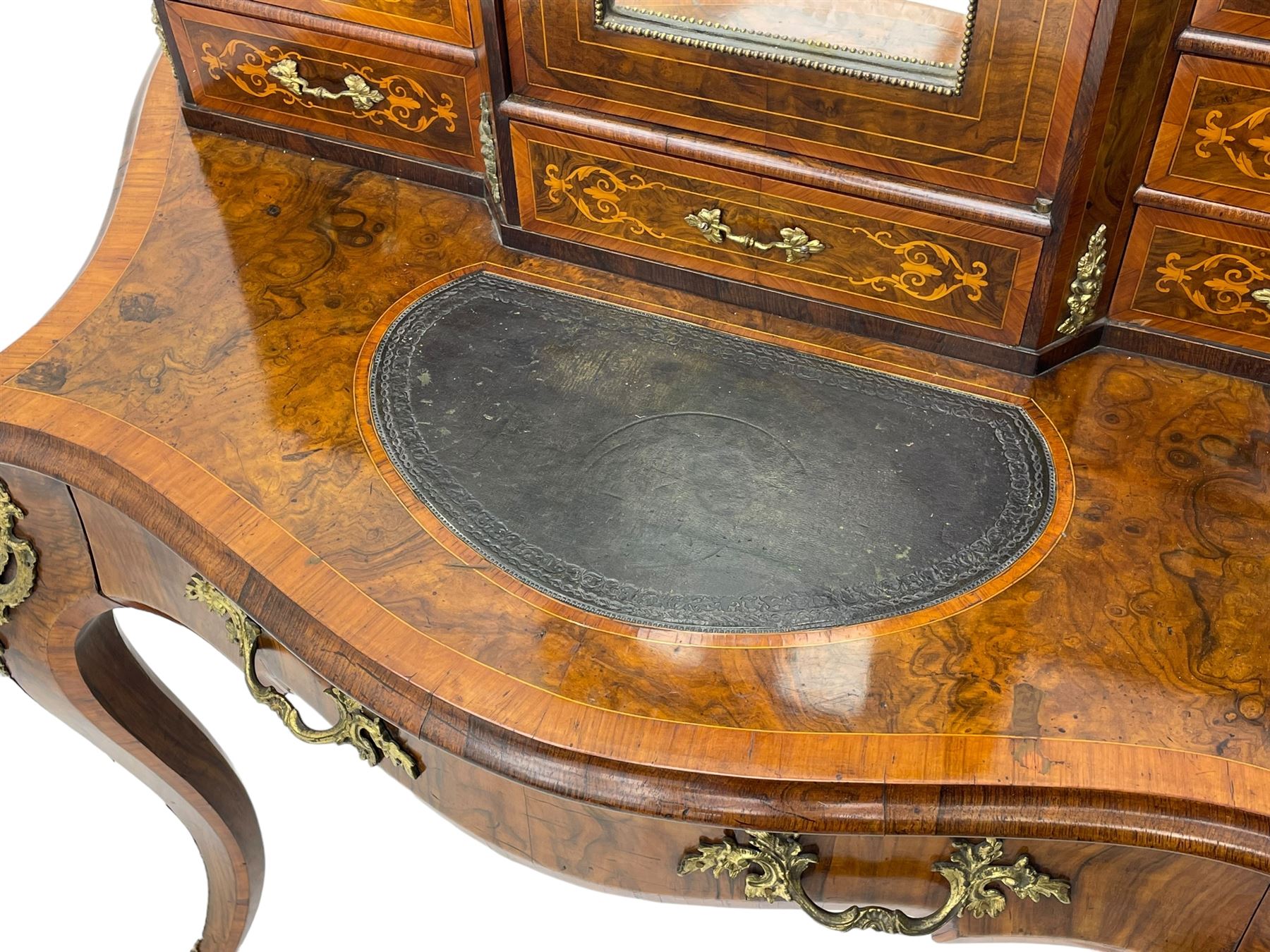 19th century French figured walnut Bonheur de Jour or writing desk, the upper section with brass gallery over mirror glazed cupboard and a combination of drawers, shaped and moulded top with leather inset and satinwood band, fitted with single drawer, on cabriole supports, inlaid throughout with scrolling foliate decoration in boxwood, ornate cast brass mounts 