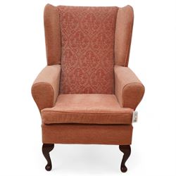 Hardwood-framed wingback armchair, upholstered in peach fabric, on cabriole feet 