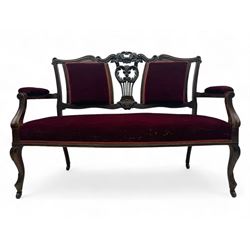 Late Victorian dark oak framed sofa, the backrests, seat and padded arms upholstered in deep red fabric, carved crest rail with scroll and foliate motifs supported by carved uprights, on cabriole supports with leaf carvings terminating in castors