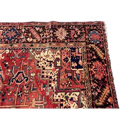 Persian Heriz red ground carpet, large central eight point medallion with projecting palmettes surrounded by small geometric motifs, decorated profusely with hooks, rosettes and animals, the busy border decorated with stylised foliate motifs within guard stripes 