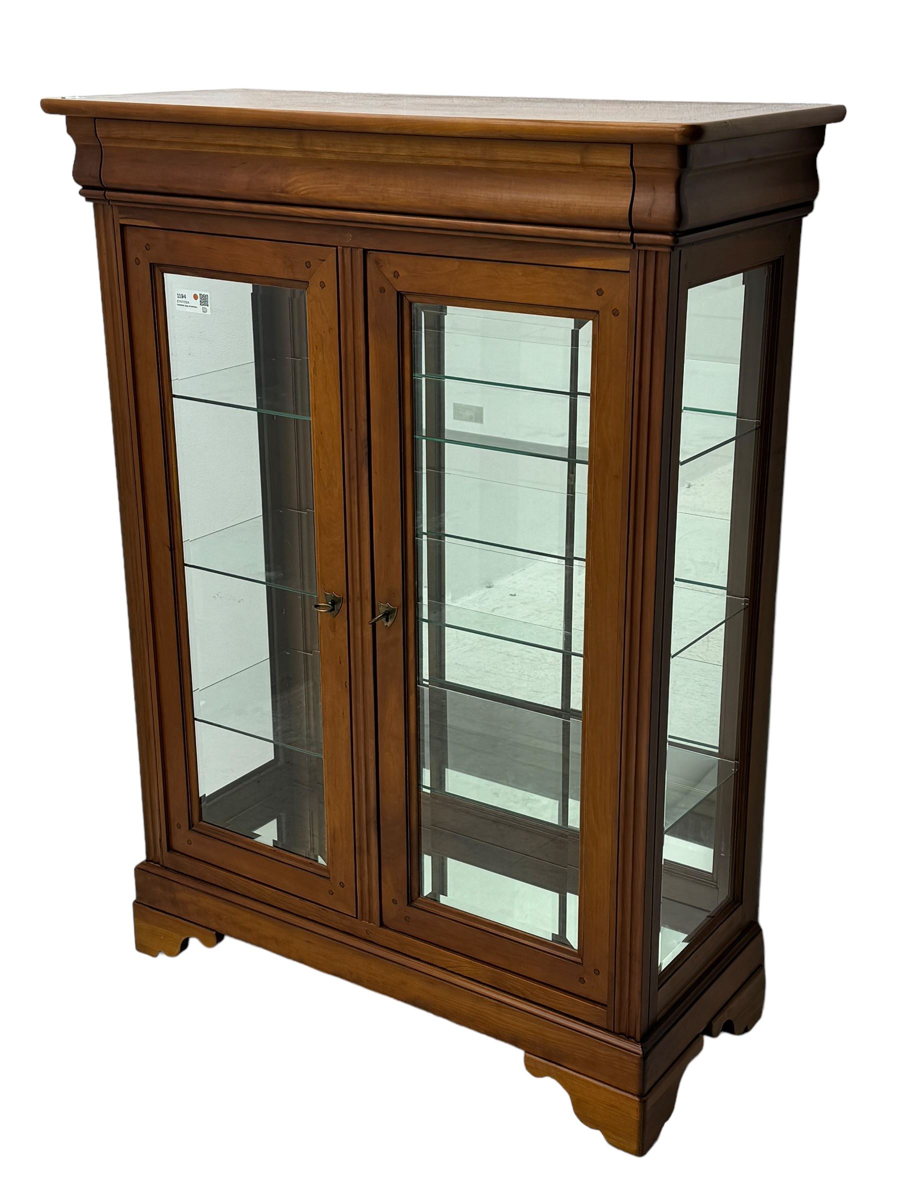 20th century cherry wood display cabinet, projecting cornice over two glazed doors with bevelled panes flanked by fluted support columns, enclosing three adjustable glass shelves with mirror-back surface, supported by shaped bracket feet