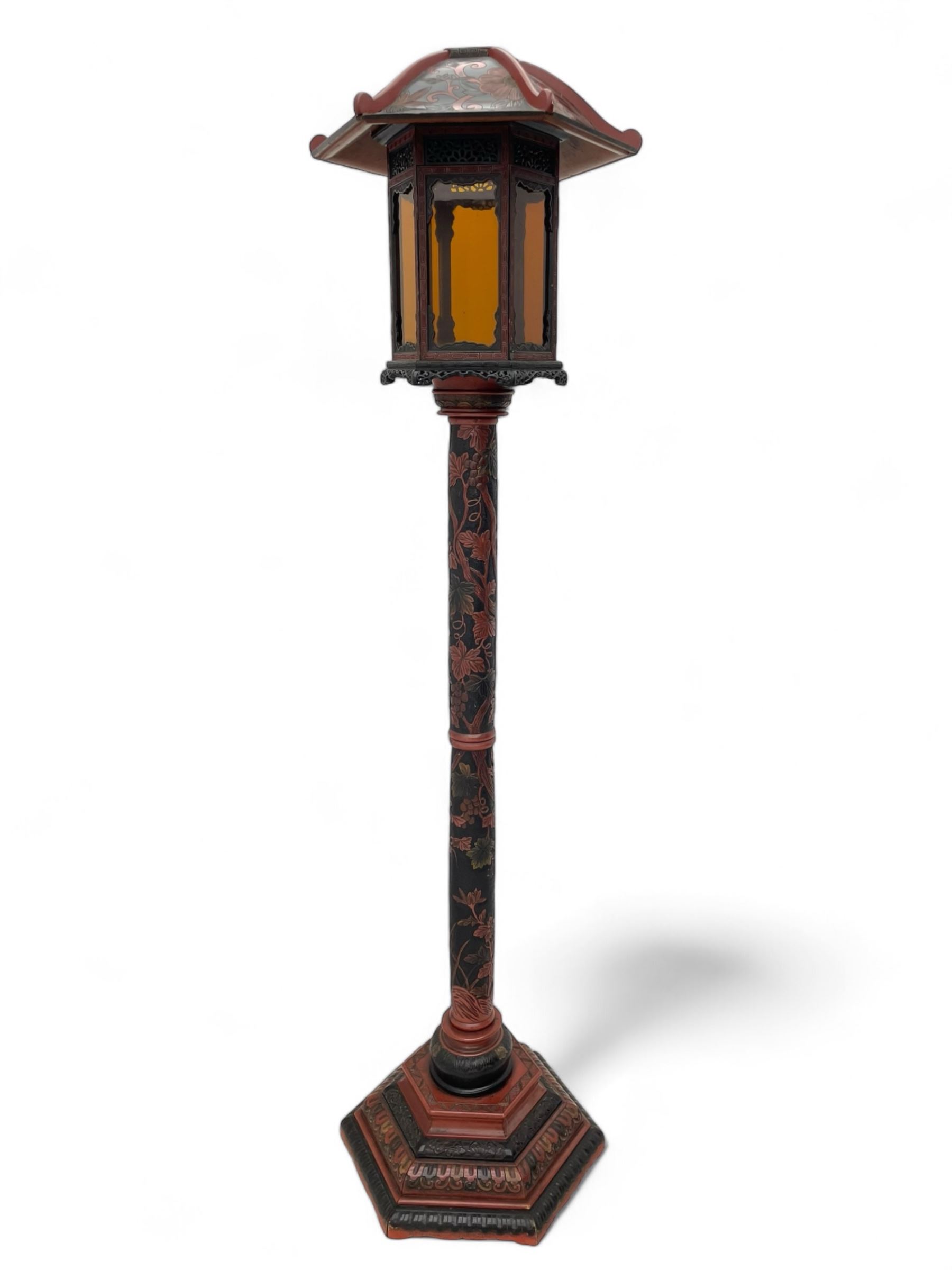 20th century Chinese black and red lacquered hardwood lantern stand, hexagonal shaped canopy top carved with flower heads and scrolls, the lantern fitted with amber tinted glass panes, pierced and carved upper panels, enclosed by two hinged doors, turned stem carved in relief with trailing vine leaves with fruits, stepped hexagonal base with carved decoration  