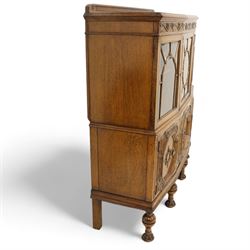 Early 20th century heavily carved oak display cabinet, frieze carved with grape vines over three astragal glazed doors with bevelled glass, over three cupboards applied with octagonal carved panels with further vine carvings, on turned and lobe carved supports