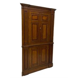 George III and later oak and mahogany banded corner cupboard, moulded cornice over four panelled doors, the door panels inlaid with mahogany bands, projecting square pilasters throughout with applied reeded mouldings, the painted interior fitted with shaped shelves, on moulded plinth base 