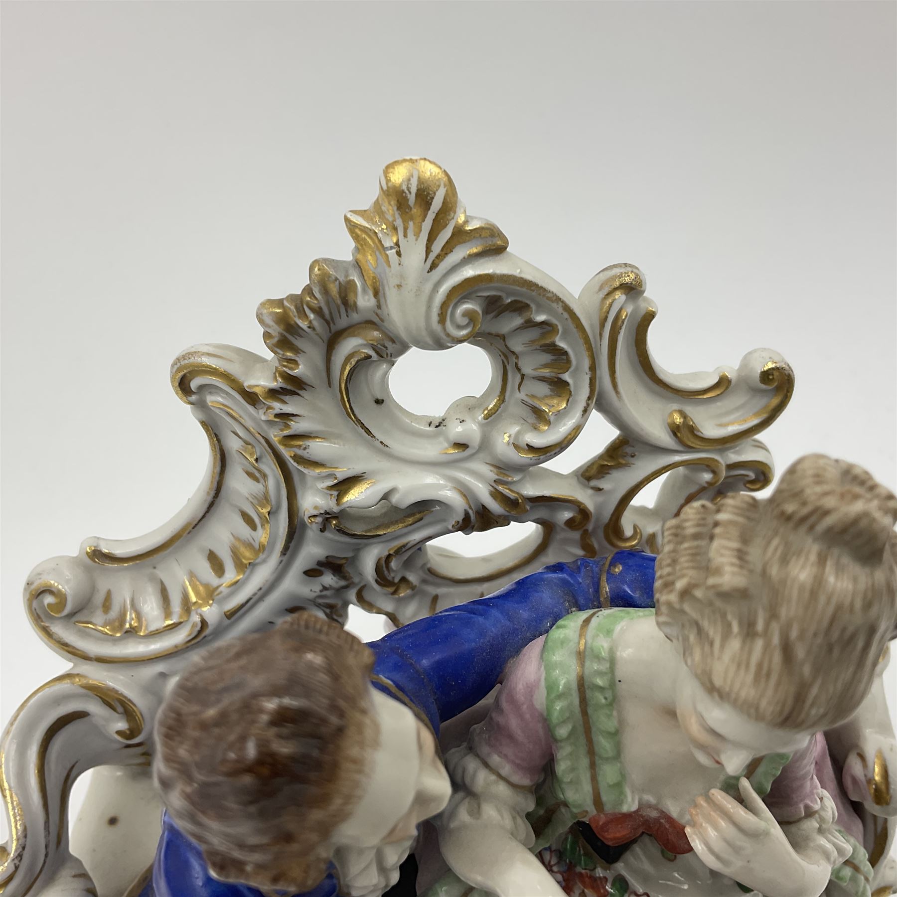 Figure group, probably Volkstedt, modelled as a courting couple seated before a table, the ornate bench and table conforming with and leading from the gilt heightened scrolling base, with blue painted mark beneath, H14.5cm
