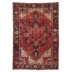 Persian Heriz red ground carpet, large central eight point medallion with projecting palmettes surrounded by small geometric motifs, decorated profusely with hooks, rosettes and animals, the busy border decorated with stylised foliate motifs within guard stripes 