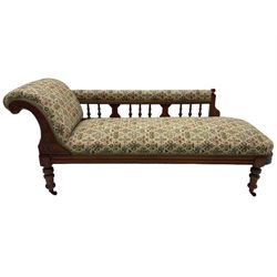 Late 19th century walnut framed chaise longue, upholstered in floral pattern fabric, rolled back rest and turned balustrade back, on turned feet with brass and ceramic castors 