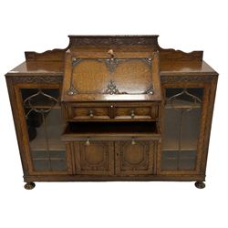 Early 20th century heavily carved oak bookcase bureau, raised back with grape-vine carved frieze, over fall-front enclosing fitted interior, above two short drawers and curved frieze drawer, flanked by astragal glazed and panelled cupboards, on turned feet