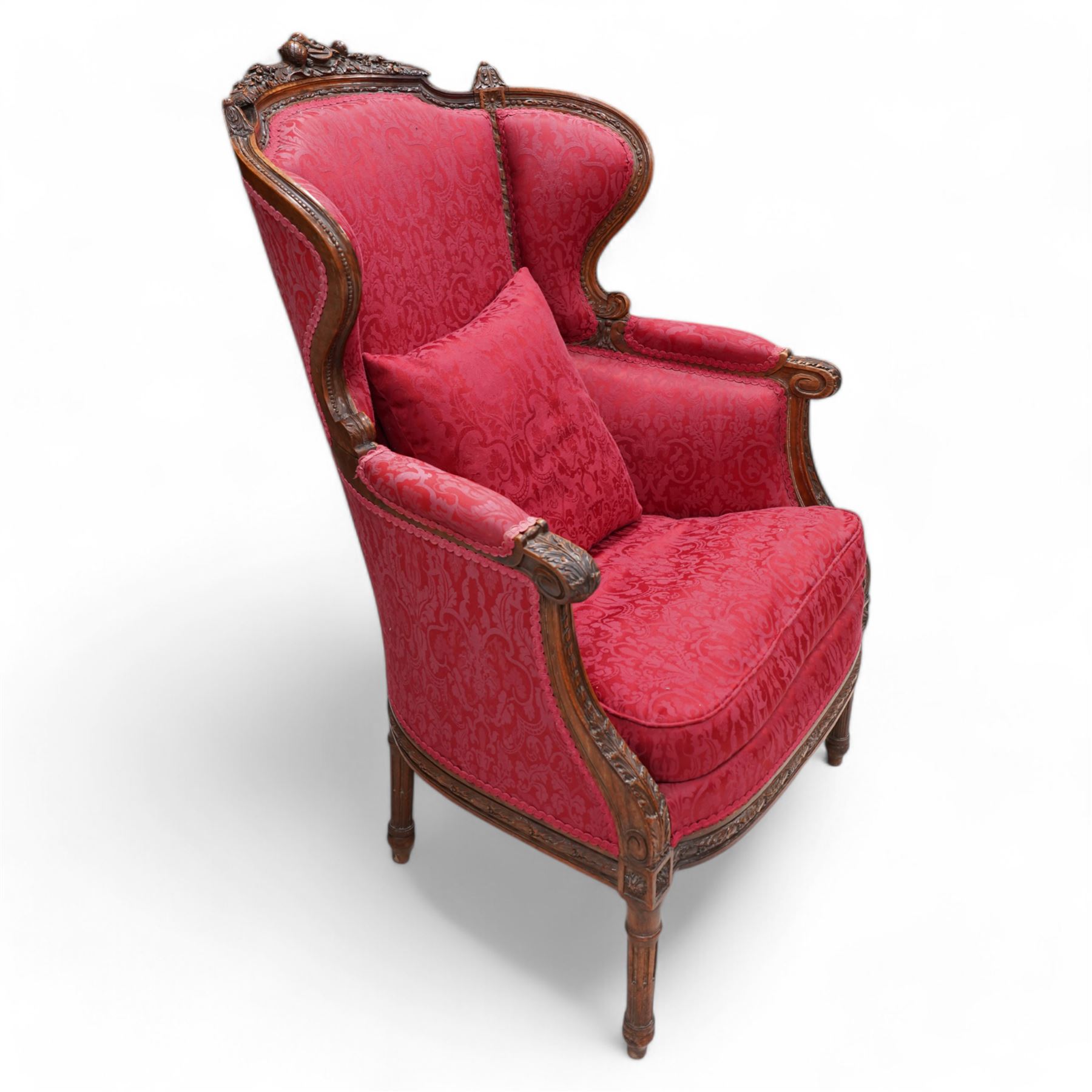 Late 19th century walnut framed fauteuil armchair, arched cresting rail carved with musical instruments and extending floral decoration, curved wing back with moulded and bead carved frame, upholstered in crimson fabric with repeating foliate pattern, acanthus carved arm terminals over acanthus and ribbon carved arm supports, the seat rail carved with fruiting foliage band, on turned and stop-fluted feet 