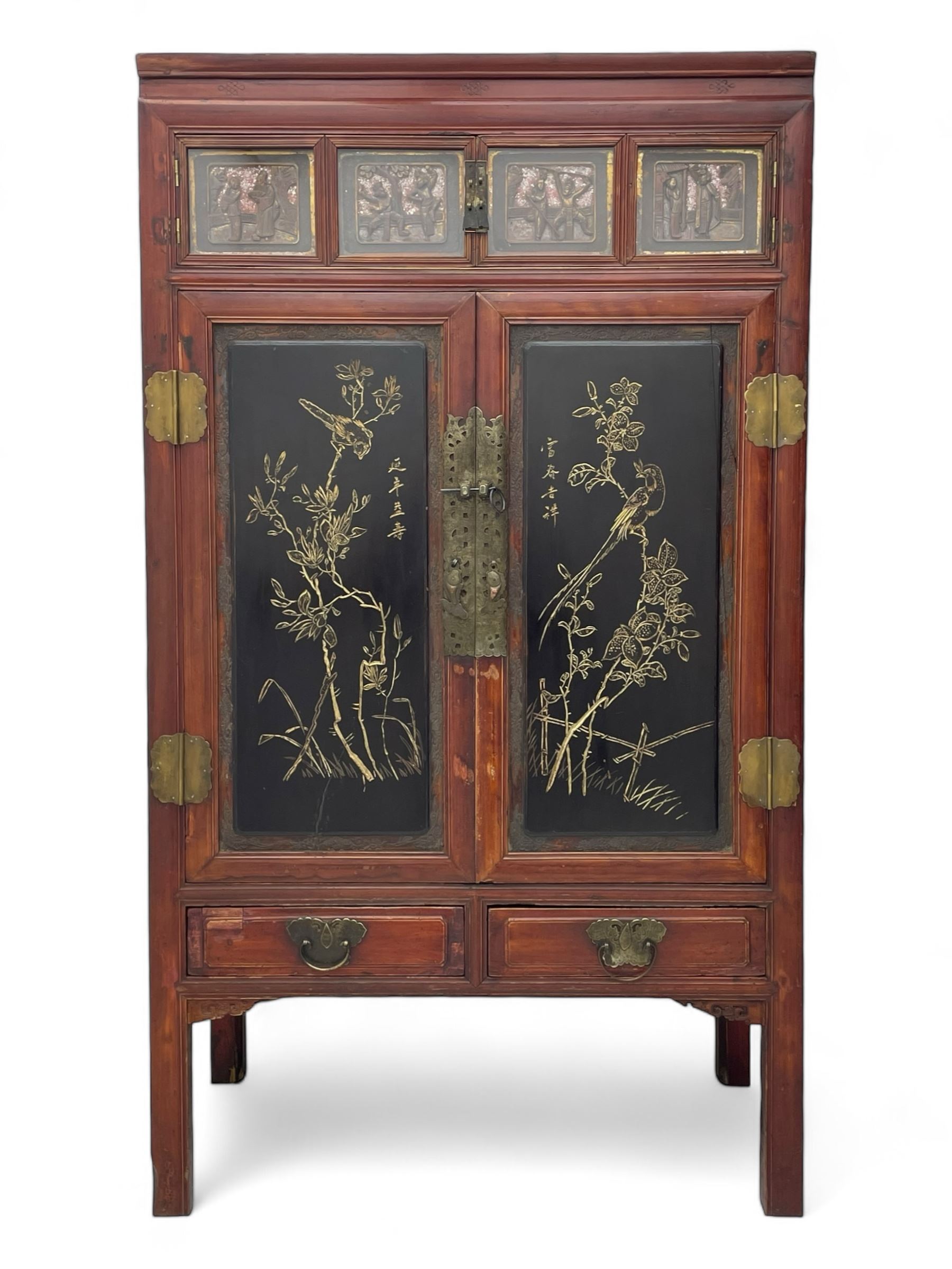 Late 19th century Chinese Qing dynasty red and black lacquered wood cabinet, Fujianese province, upper cupboard enclosed by two doors with relief carved and gilt panels depicting figures behind glass, the large cupboard enclosed by two panelled doors carved with trailing foliate branches and birds, inscribed with Chinese characters, to the left ‘Prolong life’ and to the right ‘Wealth and good fortune’, fitted with two drawers, square supports with carved brackets 