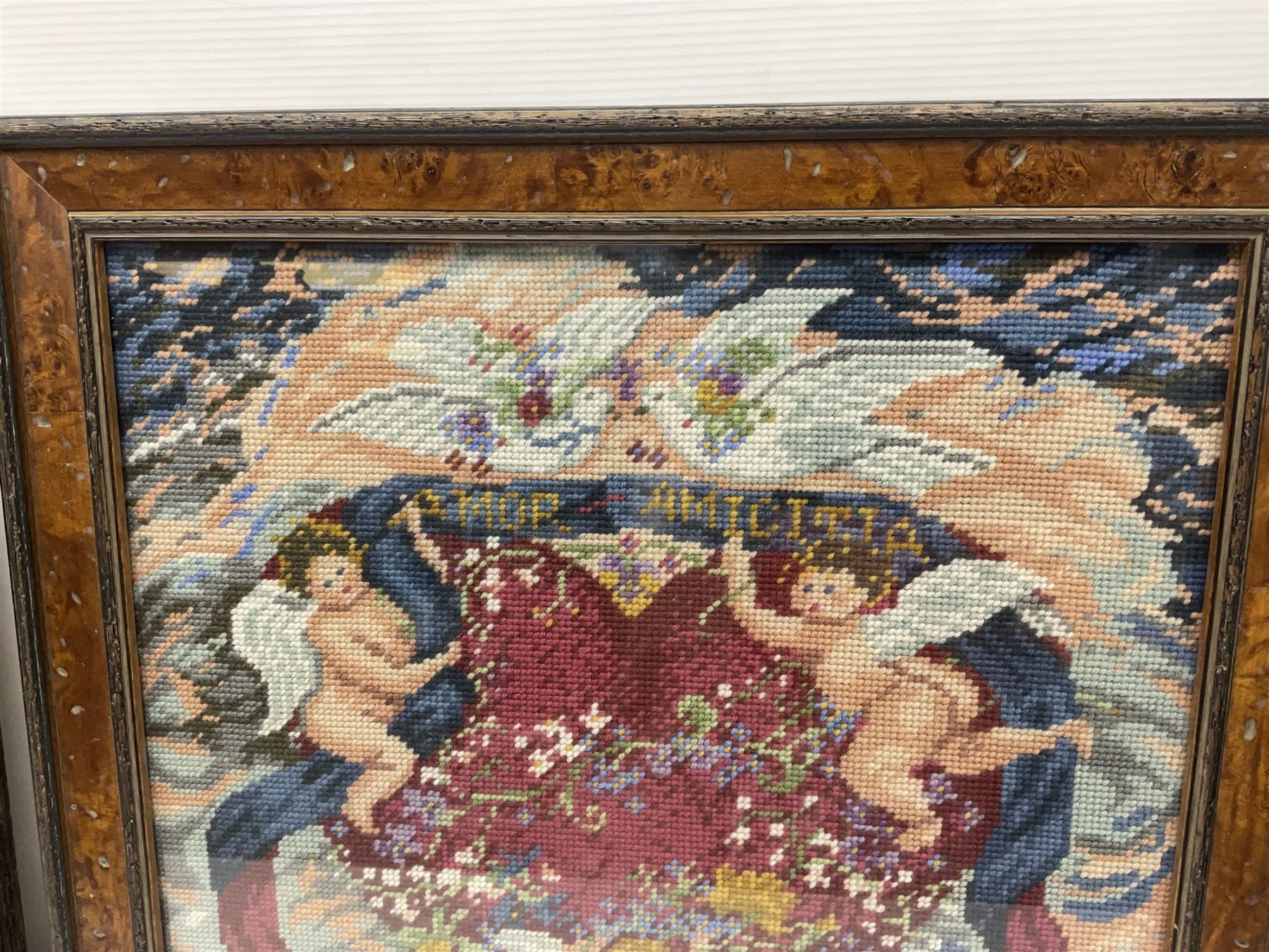 Two framed needlework samplers, the first example depicting a house and garden scene, the second cherubs