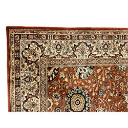 Persian design carpet, rust ground field decorated with large stylised plant motifs surrounded by smaller floral motifs, repeating trailing border