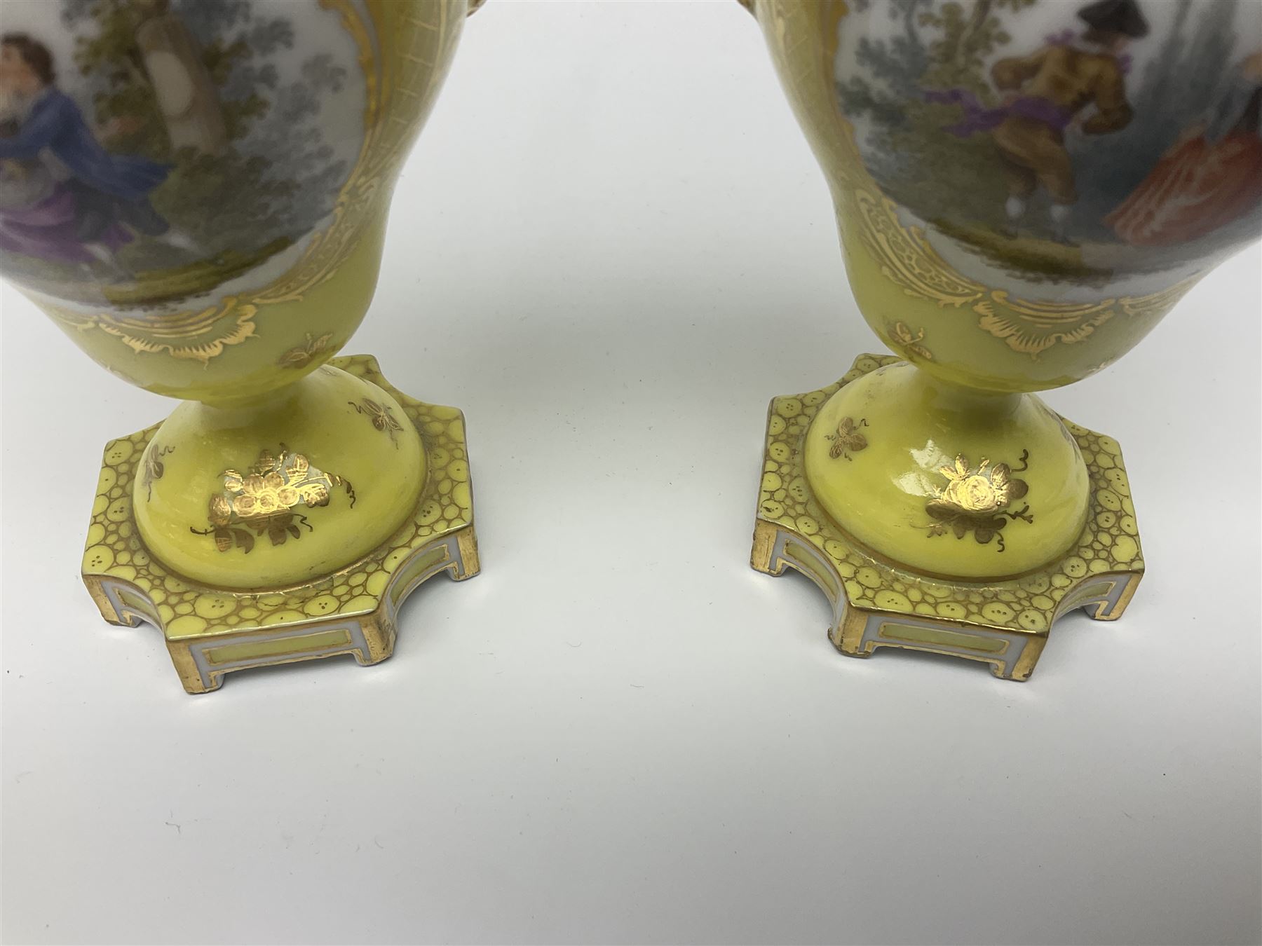 Pair of early 20th century Dresden vases with cover, of baluster form, decorated with figural panels within ornate gilt borders upon a yellow ground, with twin gilt goat mask handles, H16.5cm