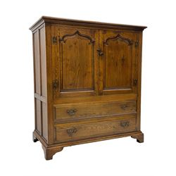 Oak drinks or media cabinet, projecting moulded cornice over two Gothic arch panelled doors on sliding tracks enclosing open storage, two drawers with brass drop handles, on bracket supports