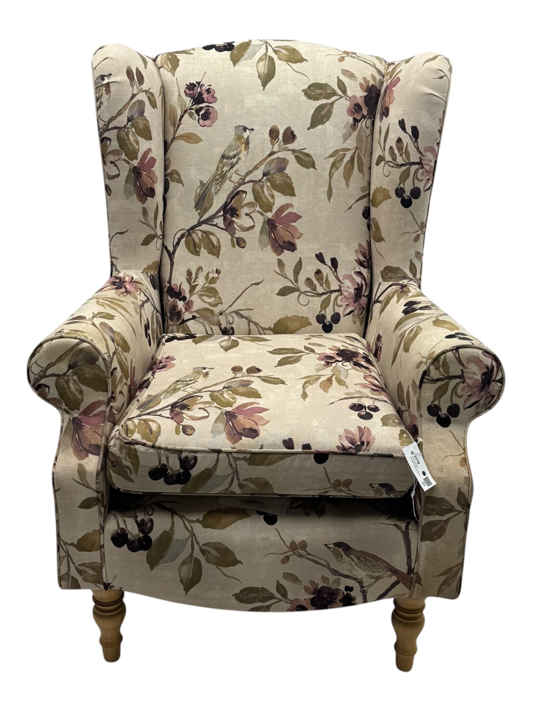 Hardwood-framed wingback armchair, upholstered in cream floral pattern fabric, on turned front feet