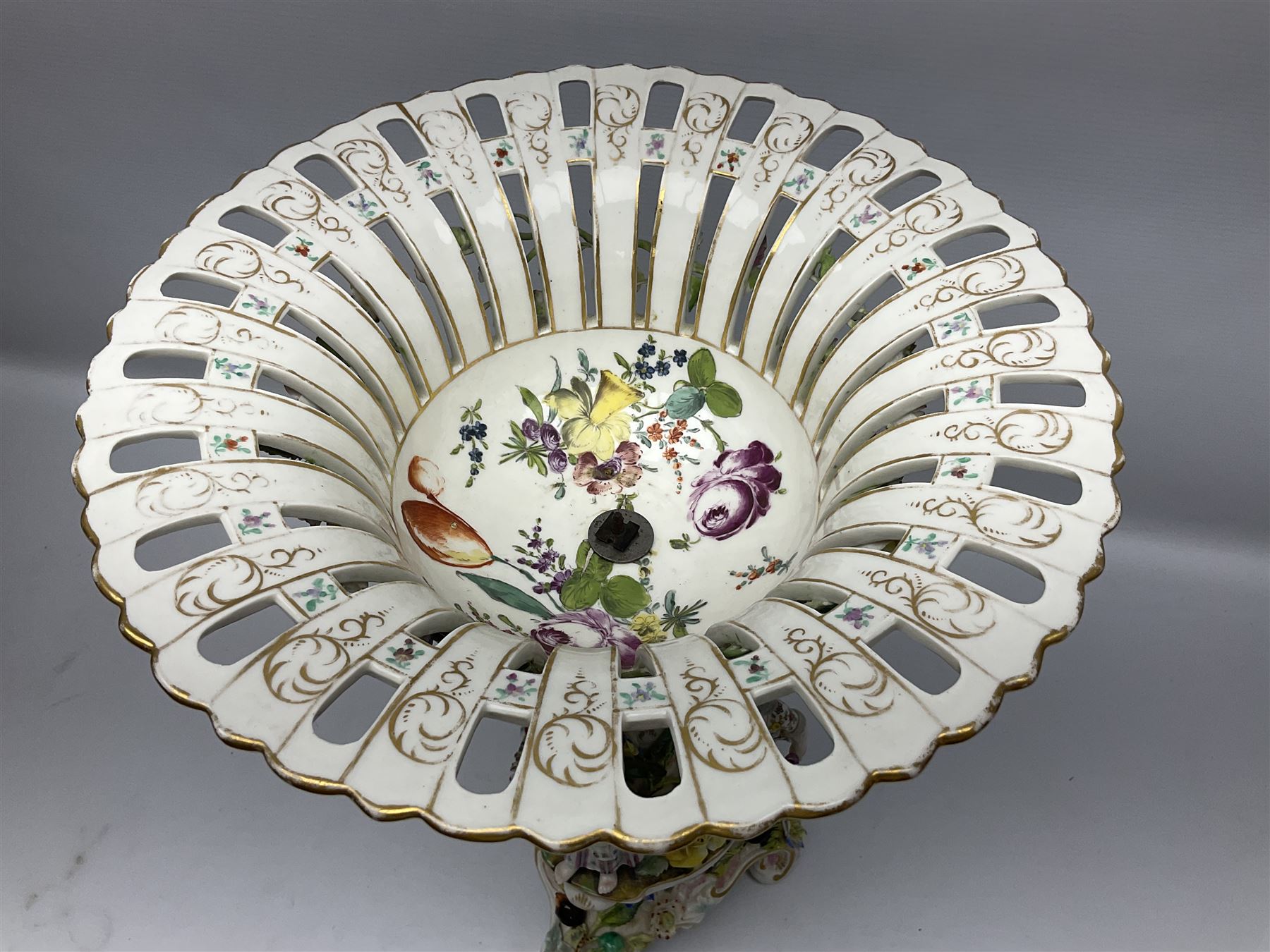 Pair of late 19th/early 20th century Continental table centre pieces, each modelled with a floral encrusted column flanked by three male and female figures with baskets of flowers, supporting a part pierced and floral encrusted bowl with hand painted floral sprays to the interior, the whole upon a conforming pierced and encrusted base with three scroll feet, each with indistinct blue mark beneath, H46cm bowl D31.5cm 