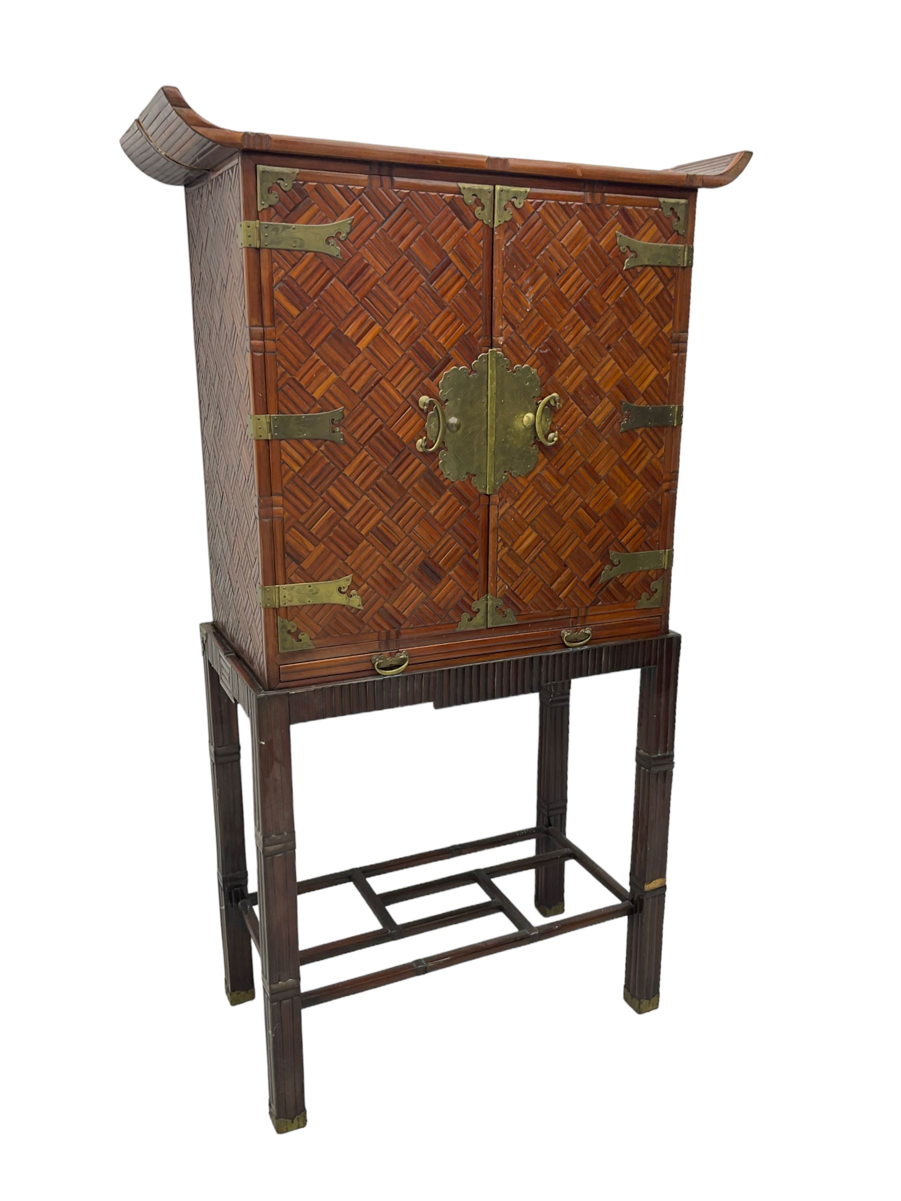 Chinese design bamboo and wood altar cabinet on stand, parquetry lattice-work bamboo, two doors with engraved metal fixtures enclosing drawers and shelf, fitted with slide, the stand pm square supports joined by a series of geometric stretchers