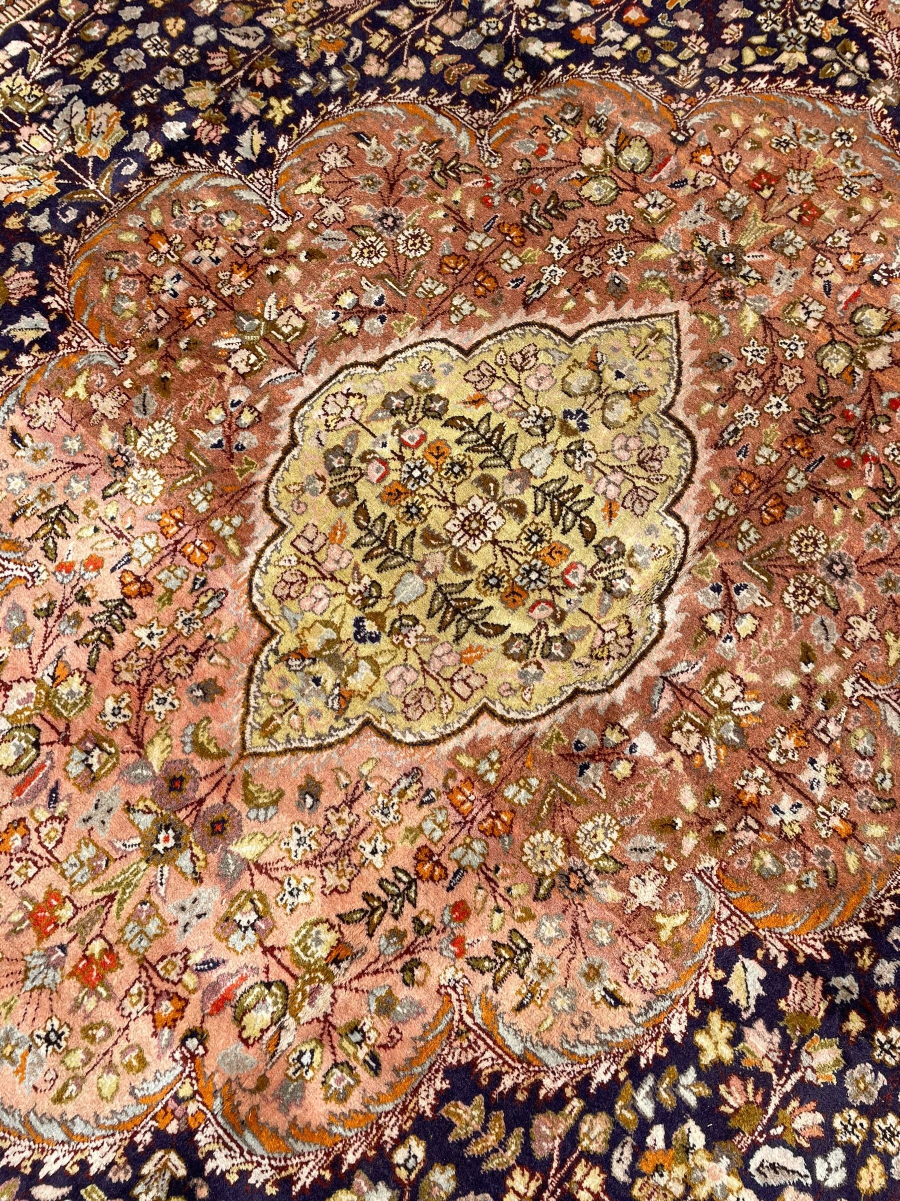 Persian Kashan, scalloped central medallion on indigo ground field, decorated profusely with branch shoots with floral motifs, pale ground spandrels decorated with stylised flower head motifs, crimson ground border decorated with repeating palmettes and trailing leafy branches, within multiple guard stripes 