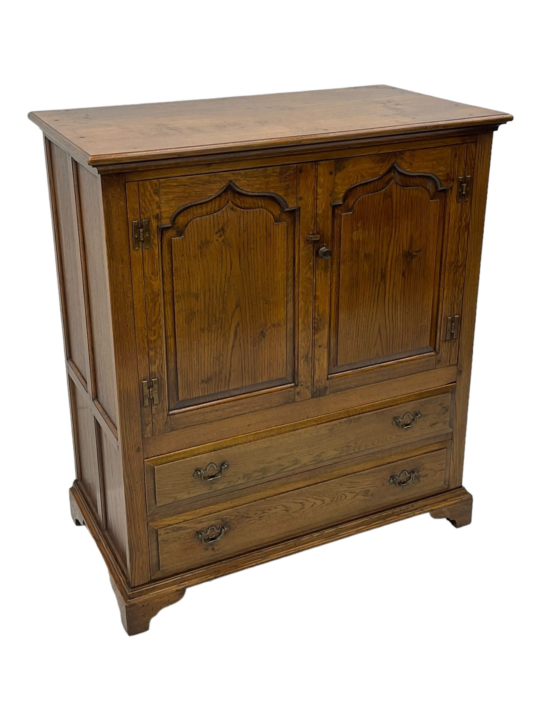 Oak drinks or media cabinet, projecting moulded cornice over two Gothic arch panelled doors on sliding tracks enclosing open storage, two drawers with brass drop handles, on bracket supports