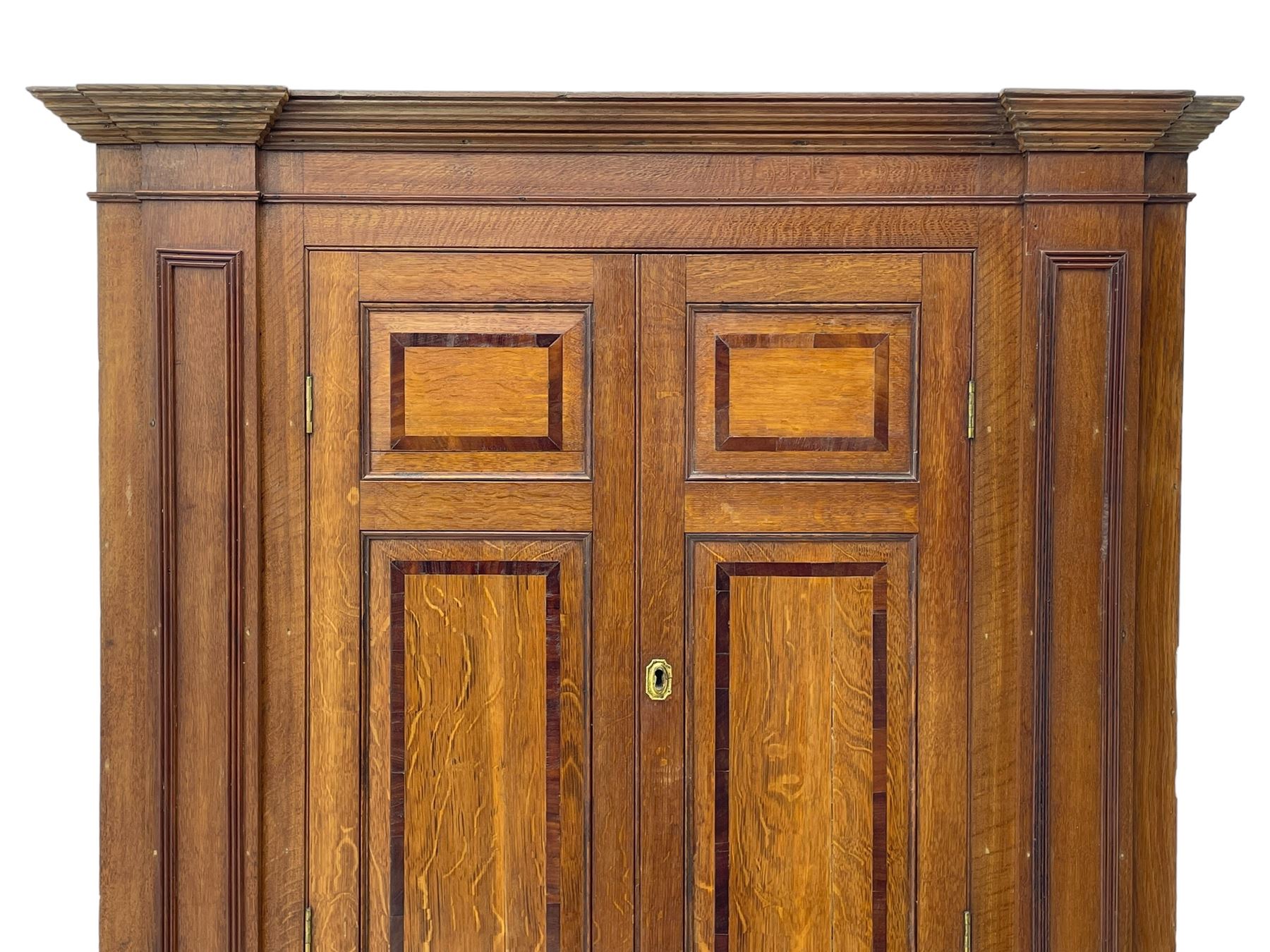 George III and later oak and mahogany banded corner cupboard, moulded cornice over four panelled doors, the door panels inlaid with mahogany bands, projecting square pilasters throughout with applied reeded mouldings, the painted interior fitted with shaped shelves, on moulded plinth base 