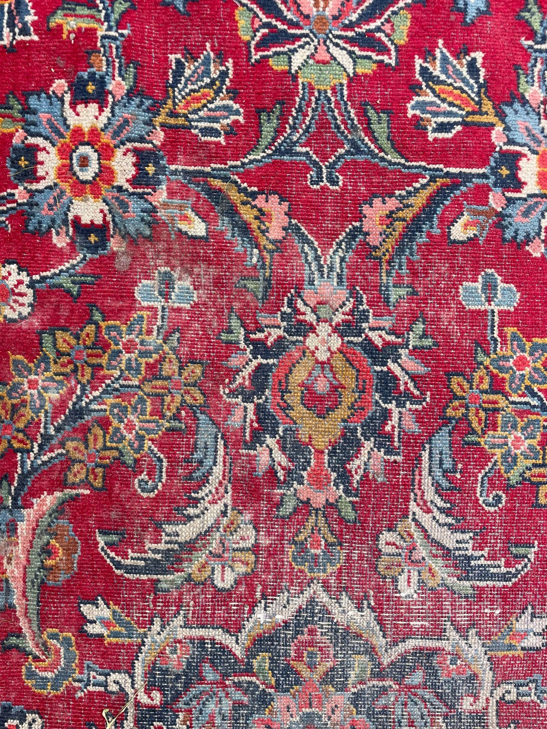 Large Persian Kashan crimson ground carpet, central floral medallion surrounded by swirling leafy branches and palmettes, enclose by floral pattern spandrels, the indigo border with overall scrolling design decorated with palmettes, within guard stripes 