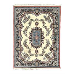 Persian design ivory ground rug, the field decorated with an oval medallion filled with floral motifs and scrolling vines, flanked by floral sprays and corner spandrels with palmette designs, the main border featuring a series of stylised floral patterns against a dark blue ground, enclosed by multiple guard stripes with geometric and floral motifs