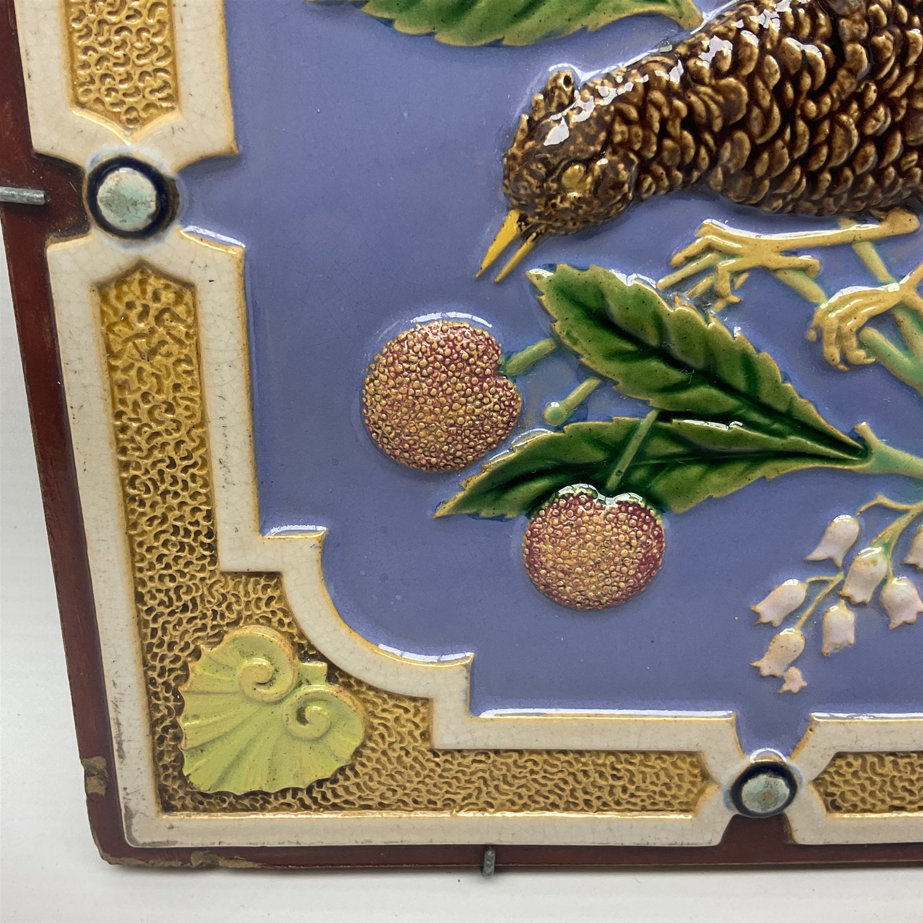 19th century Minton & Co majolica tile, decorated in relief with a bird upon a fruiting branch against a blue ground, with textured ochre border and anthemion to each corner, impressed mark verso, H19.7cm