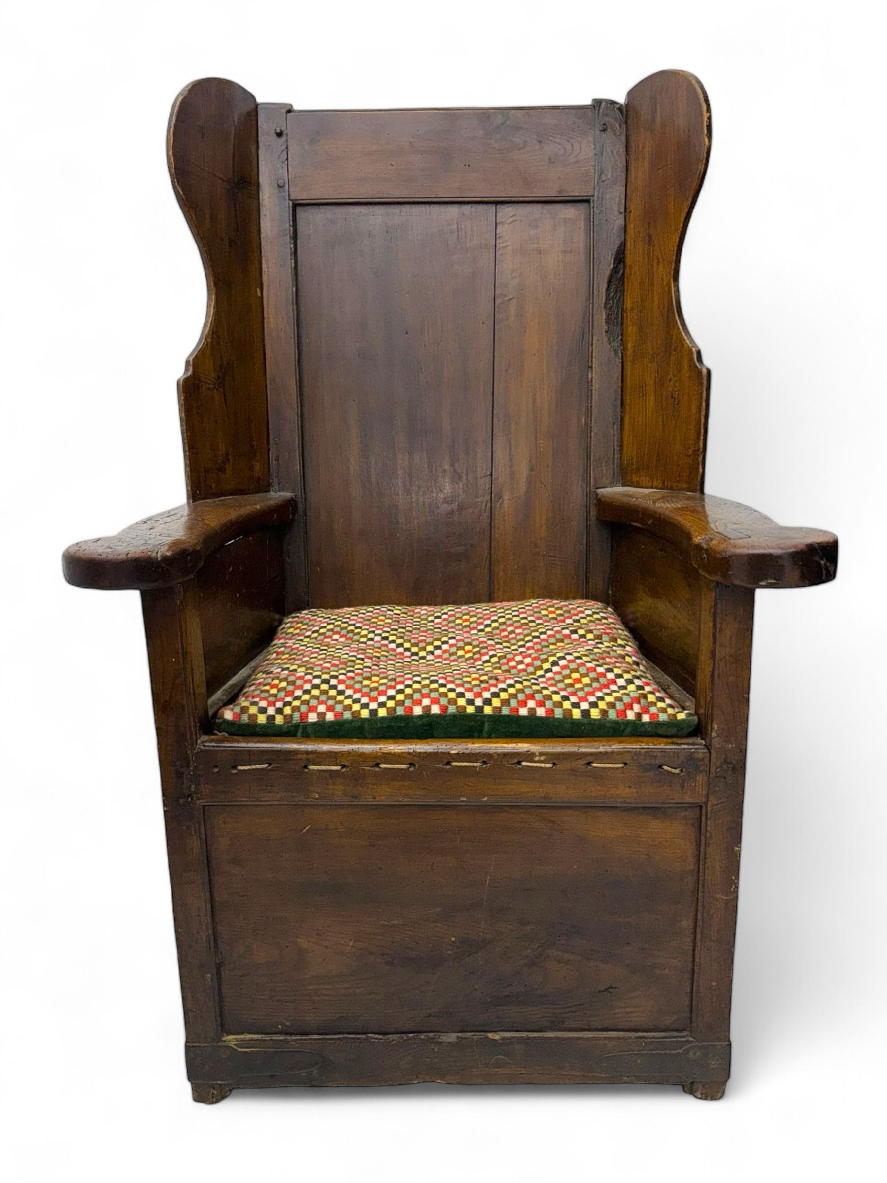 George III oak lambing chair, tall rectangular panelled backrest with shaped wings over broad scrolled armrests, box seat with removable geometric upholstered cushion, integrated drawer to lower section, resting on square supports