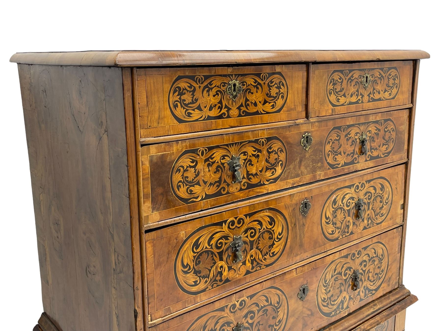 18th century inlaid walnut chest on stand, ovolo-moulded rectangular top inlaid with ebony panels each decorated with scrolling foliage, flower heads and birds, fitted with two short over three long drawers, the drawer fronts decorated with ebony panels enclosing curled leaf inlays, the base fitted with single drawer on turned supports united by waved stretchers, on turned bun feet 