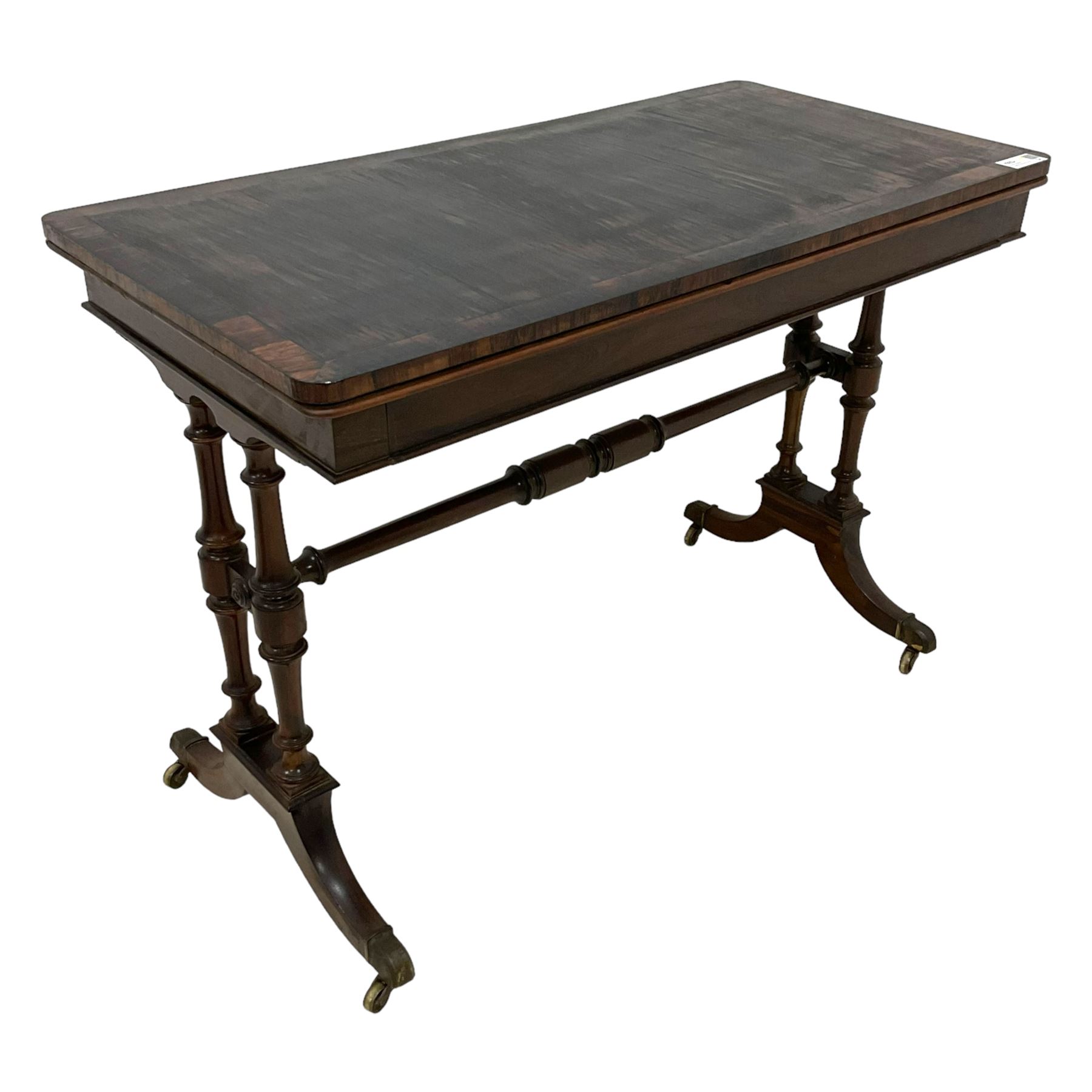 Regency rosewood card table, fold-over swivel action rectangular top with crossbanding, single frieze drawer, raised on turned end supports terminating in splayed feet with castors, joined by ring turned stretcher