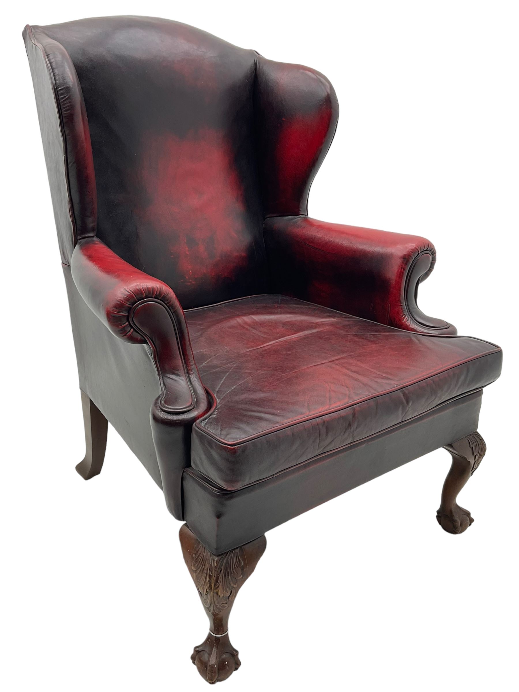 Georgian design hardwood-framed wingback armchair, upholstered in red leather, loose seat cushion and rolled arms, on acanthus carved ball and claw front feet 