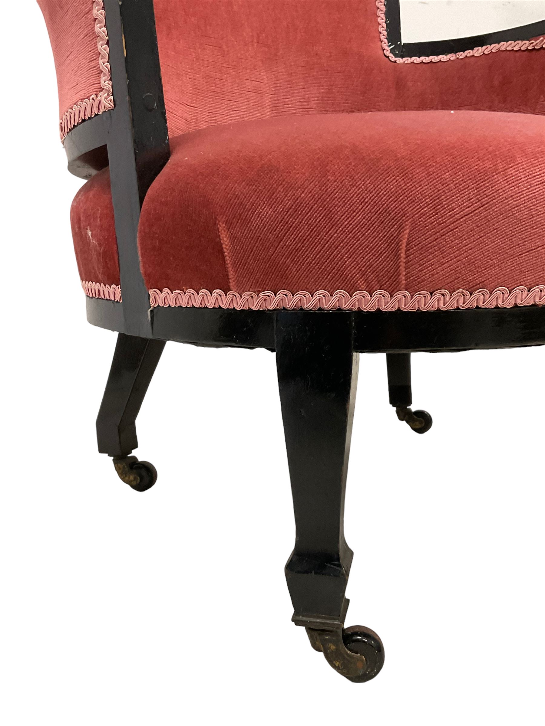 Early 20th century ebonised hardwood-framed armchair, rolled back and curved arms, upholstered in pink fabric, on square tapering front supports with spade feet, brass and ceramic castors 