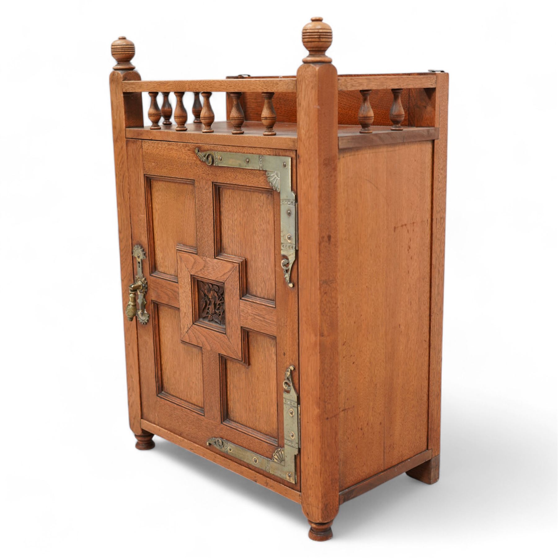 Late 19th century Aesthetic Movement walnut cupboard, raised and pierced spindle gallery surmounted by ring-turned finials, over a panelled door decorated with central foliate carved panel and surrounded by plain geometric shaped panels, applied with brass fittings and loop handle, on turned feet