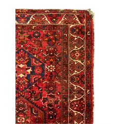 Persian Hamadan rug, red ground with overall geometric design, the field with three extended lozenges, decorated with geometric and stylised flower head motifs, the border and guards decorated with repeating geometric motifs