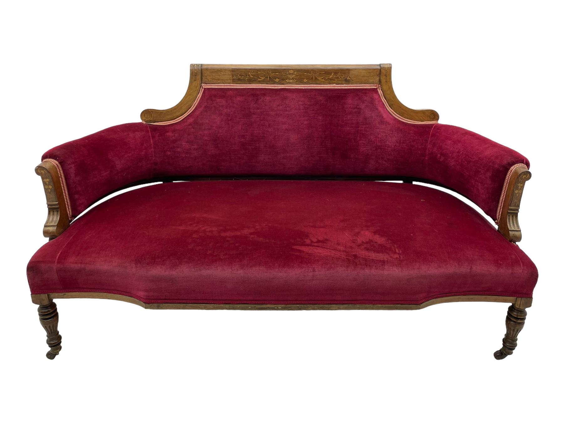 Late Victorian inlaid walnut two seat settee, the shaped cresting rail decorated with foliate inlays and boxwood stringing, upholstered in crimson velvet with sprung seat, raised on turned and fluted supports with ceramic castors