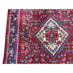 Persian Herati crimson ground rug, the busy field decorated with a central lozenge medallion surrounded by interlocking Herati motifs, the indigo guard band with repeating palmette and stylised plant motifs